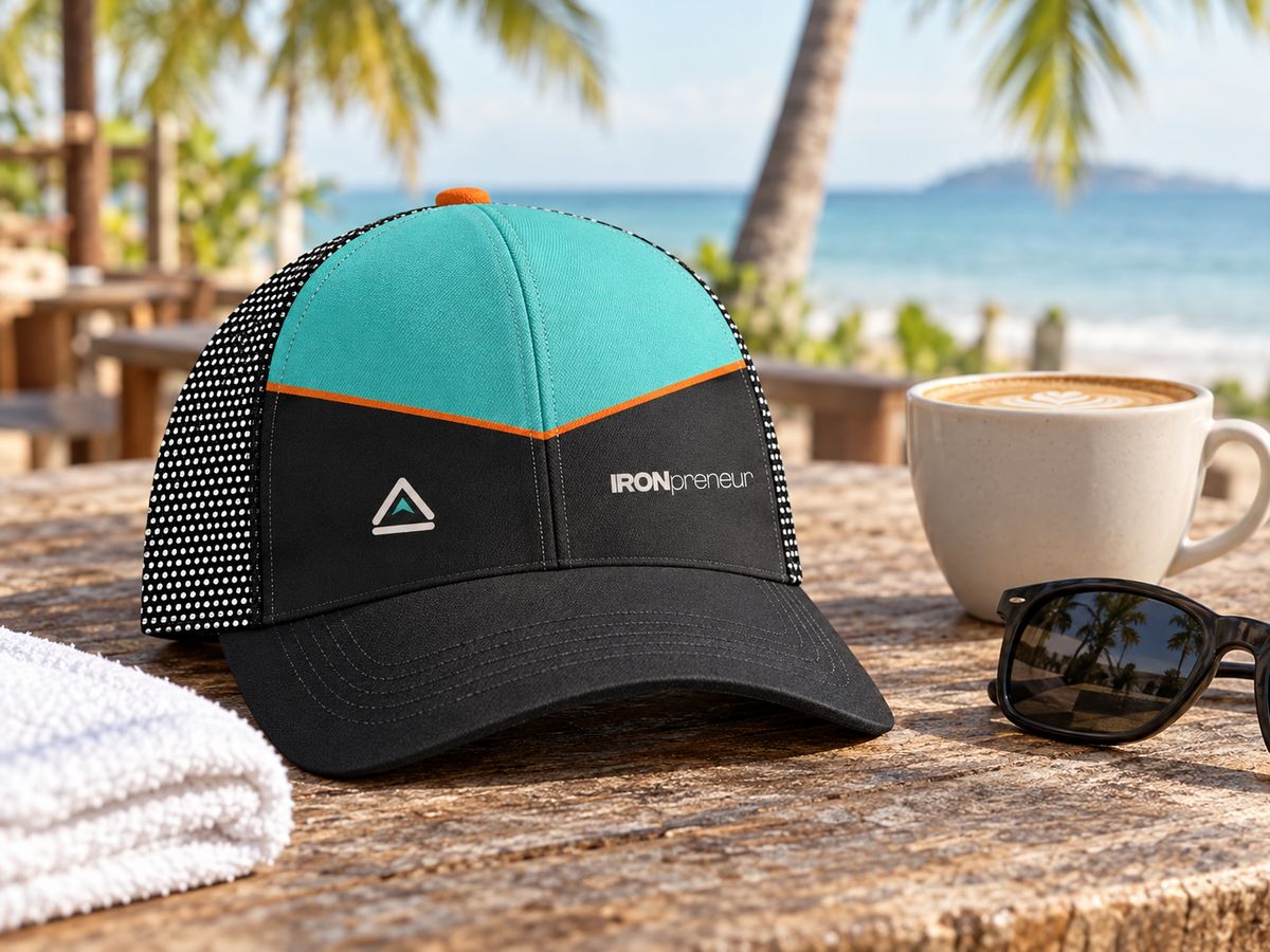 Concept render: the trucker cap on a café table by the sea next to a flat white and sunglasses.